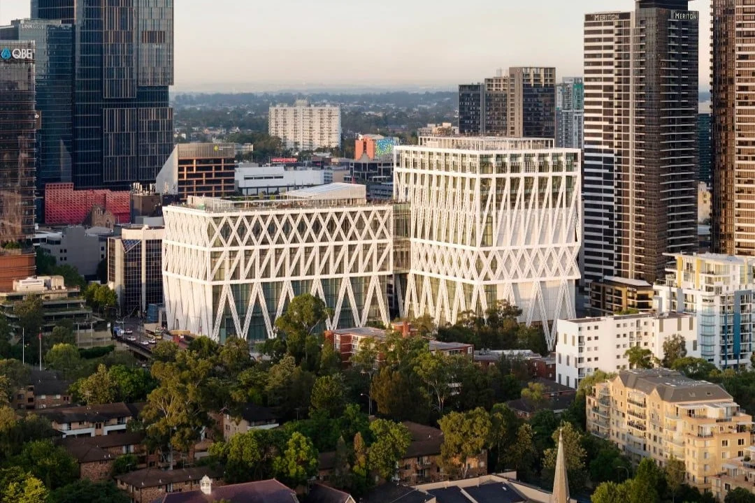 Aerial view of twin modern high-rise buildings with striking white diamond-pattern facades, surrounded by trees, homes, and downtown towers.
