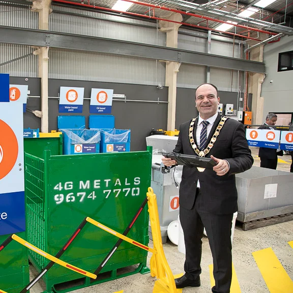 A man in a suit and chain stands smiling in an electronic waste facility.