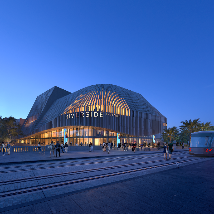 Modern theater building at dusk with glowing windows and sleek, curved design. People gather outside; a tram approaches on nearby tracks.