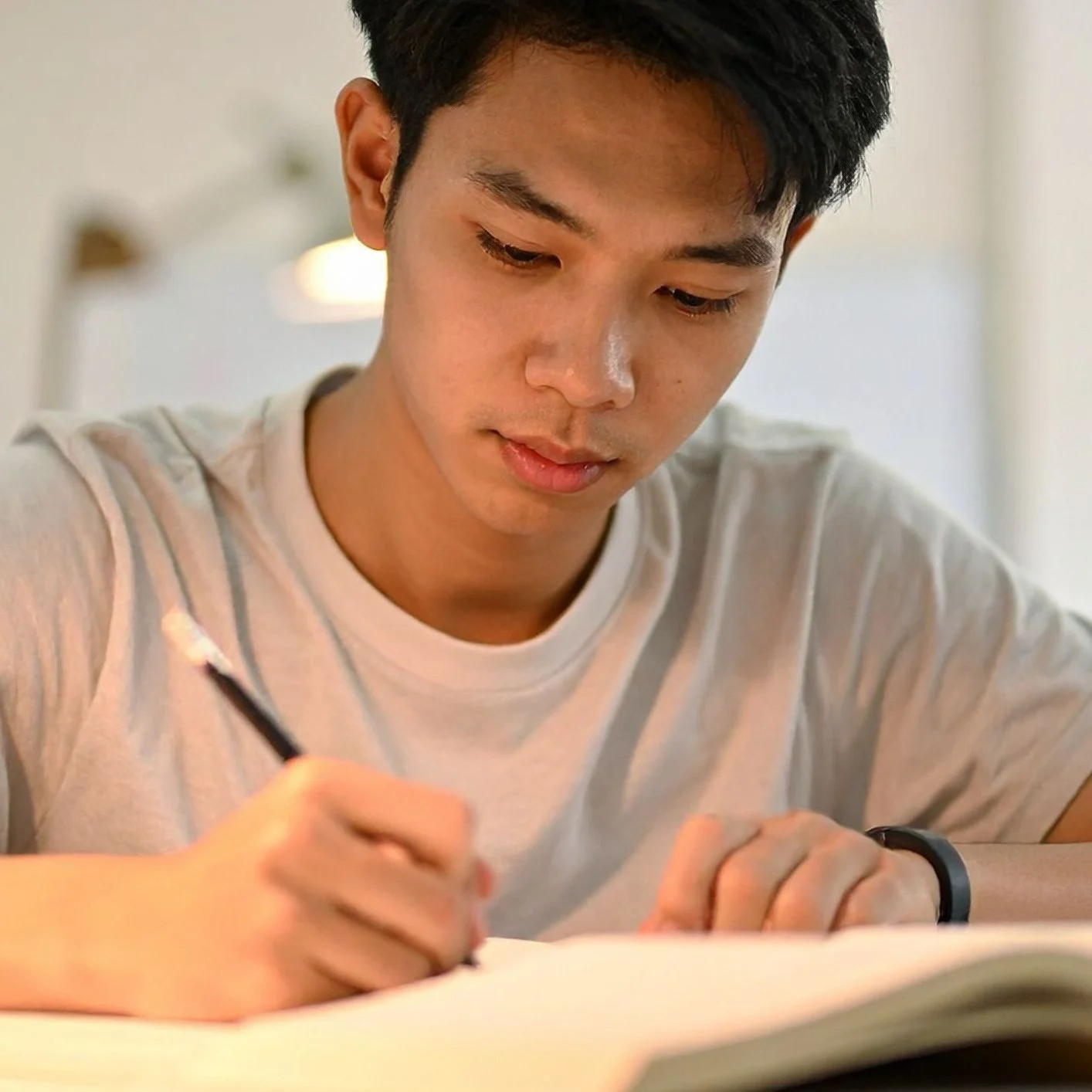 Man in white tshirt holds black pencil on open workbook.