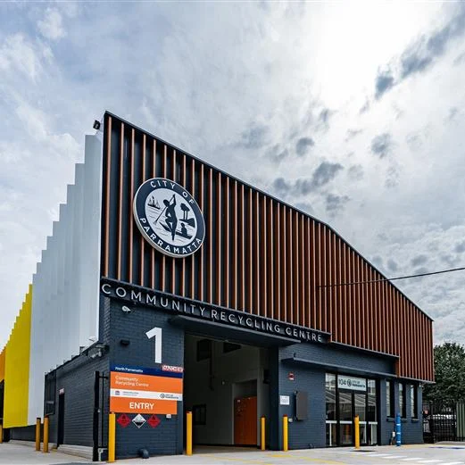 Modern recycling center with colorful, geometric facade and prominent city logo under a cloudy sky. Entry signs indicate the welcoming entrance.