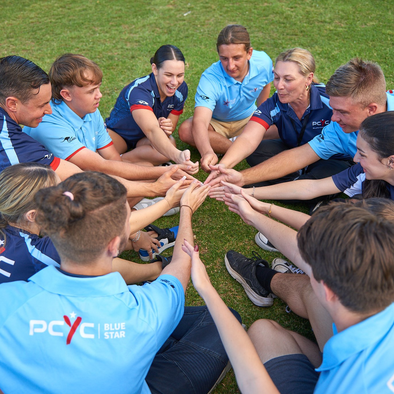 Group of people in PCYC jerseys with hands in middle of circle