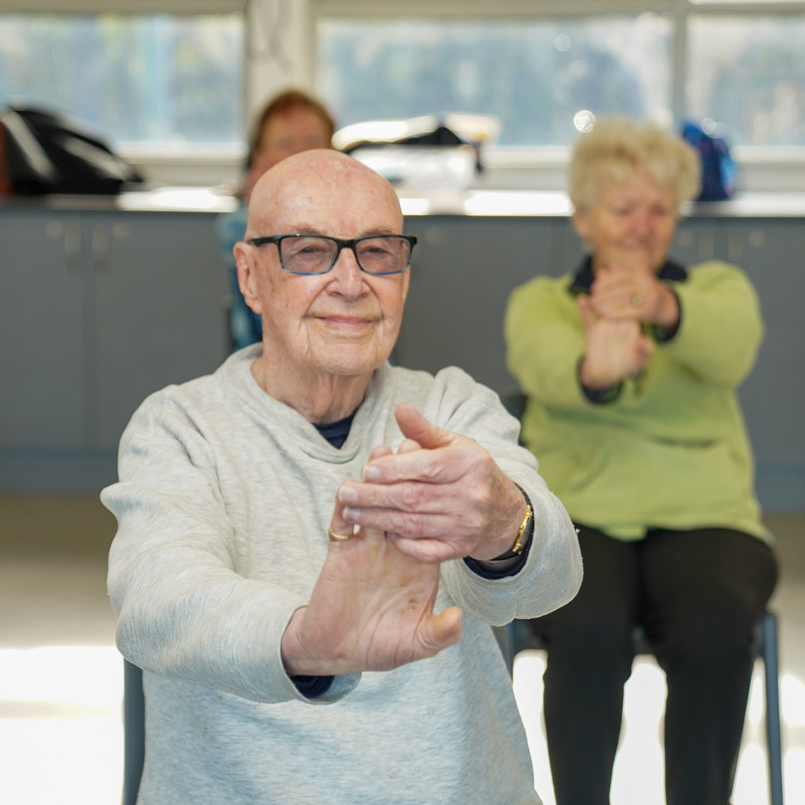 Elderly people sitting on chairs exercising