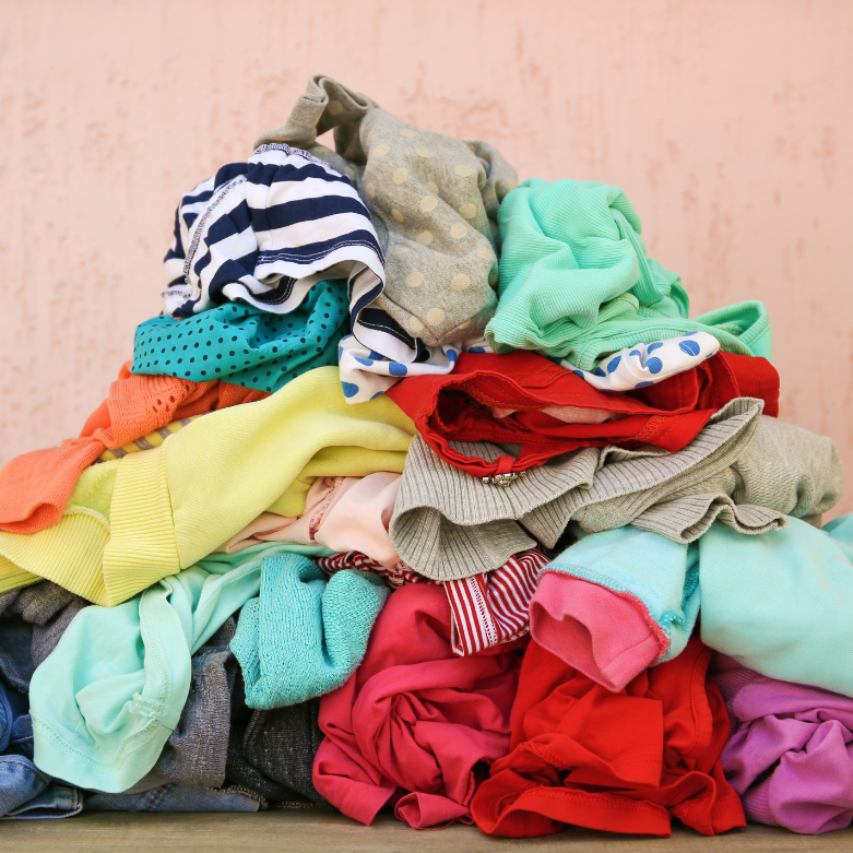 A colorful, large pile of various clothing items, including striped, polka dot, and solid patterns, is stacked against a peach wall, conveying clutter.