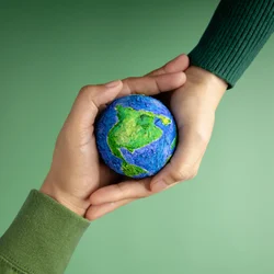 Two hands gently cradle a small blue-and-green Earth against a soft green background, symbolizing care for the planet and environmental protection.