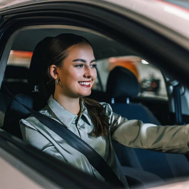 Woman in grey long sleaved shirt sitting in drivers seat of car, with red lipstick.