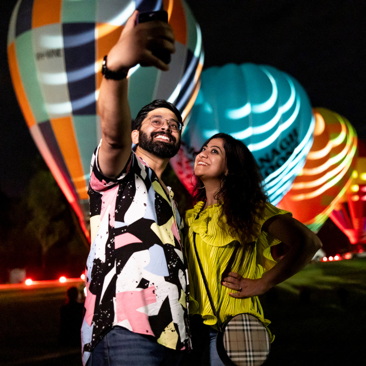 A man and a woman taking a selfie with hot air ballons in the background